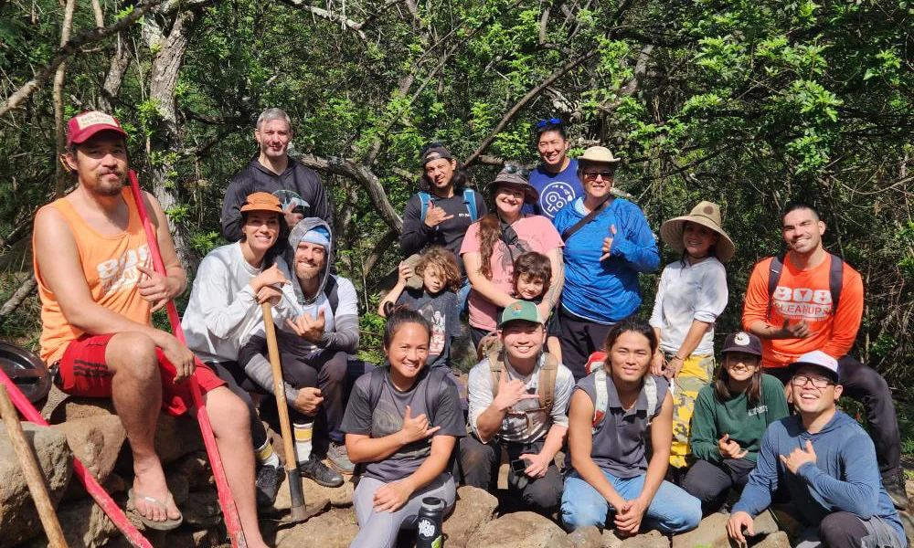 A community work day gathered for a photograph, tools in hand on a forest trail